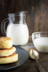 Pancake cheese with a jug and a glass of milk for breakfast on a gray plate, in a rustic style, close-up, shallow depth of field, selective focus. Concept, healthy homemade food.