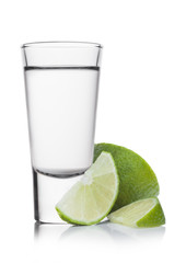Glass shot of silver tequila with lime slices on white.