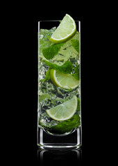 Highball glass of Mojito summer alcoholic cocktail with ice cubes mint and lime on black.