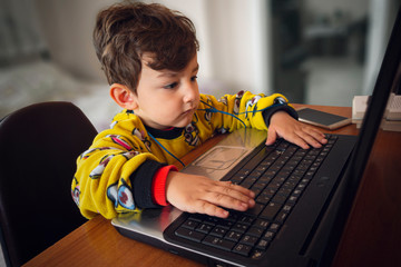 3 years old cute boy with yellow pajamas using laptop