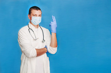 Doctor proctologist on a blue background in a white coat, gloves and a surgical mask looks at the...
