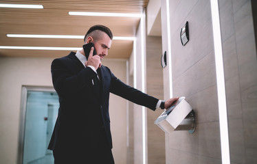 Businessman calling while looking and leaning on touch panel of elevator in office