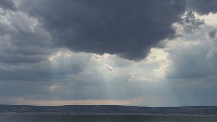 the sun's rays penetrate the dark storm clouds and birds fly past them