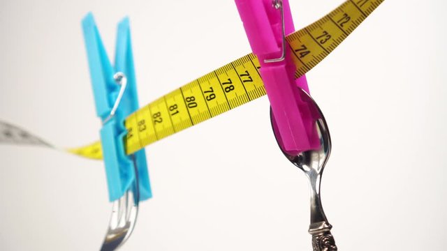 spoon and fork are fixed with blue and pink clothespins on a yellow white centimeter on a white background. Shiny cutlery swaying. Diet fasting concept