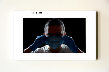 a white tablet lies on a beige table on the screen image of a silhouette of a man putting on a medical mask in sterile gloves, stay home save the world of the coronavirus epidemic strain covid-19.