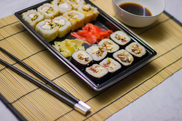 Fototapeta na wymiar japanese cuisine different rolls with black chopsticks red pickled ginger wasabi sauce and soy sauce on the table