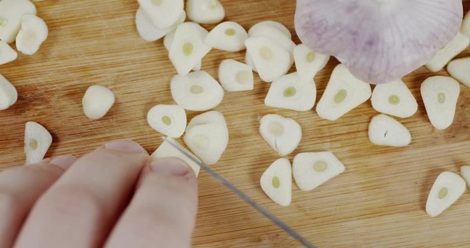 Man's hand cut garlic with a knife on a cutting Board.