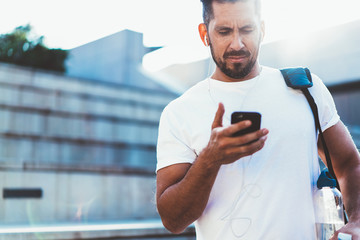Pensive caucasian hipster guy checking notification about downloading new music on smartphone for...