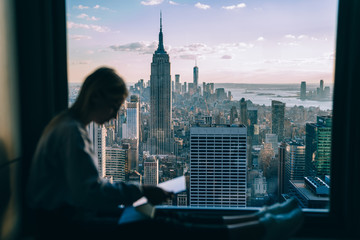 Selective focus on cityscape scenery from highrise panoramic window with millennial woman using modern technology on blurred frontage, above view from building on Manhattan district in New York