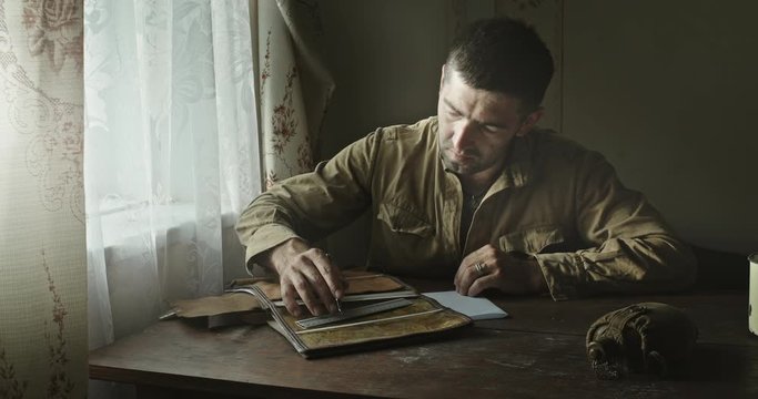 A Soviet Army soldier sits at a table in an abandoned farmhouse and looks at a map of the area. Reconstruction of the events of World War II intelligence soldier.