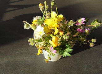 Bouquet of simple wildflowers in a plastic glass on a dark background, indoor, close up