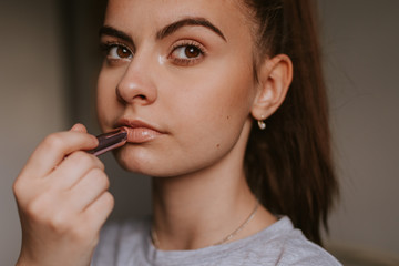 Portrait of a young caucasian girl putting lipstick on her mouth