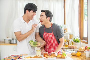 Obraz na płótnie Canvas Happy young Asian homosexual gay couple eat breakfast meal together in the kitchen. Handsome guy LGBTQ lover enjoy with romantic lifestyle at home. Same-sex marriage and LGBT relationship concept. 