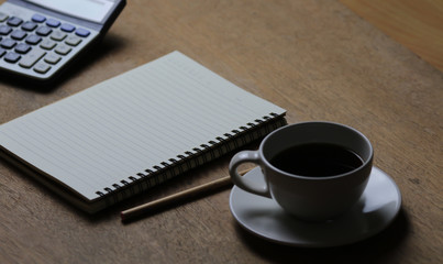 Notebook, white coffee cup and pencil on wooden table. Selective focus.