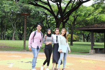 Fototapeta premium Young asian malay chinese man woman outdoor park walk stand study talk discuss point laptop file book backpack mingle fun happy