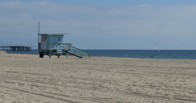 Lifeguard hut on a deserted beach with a pier and sailboat in background