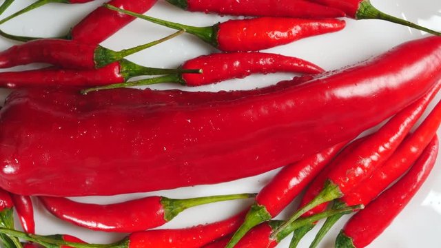 Top View Of Fresh Raw Red Chili Peppers And Ramiro Pepper With Water Drops Rotating On A White Plate.
