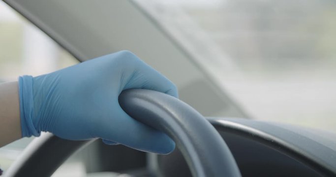 Hands in gloves on steering wheel driving car covid 19 pandemic crisis