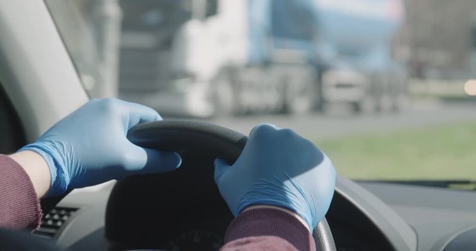Hands in gloves on steering wheel driving car covid 19 pandemic crisis