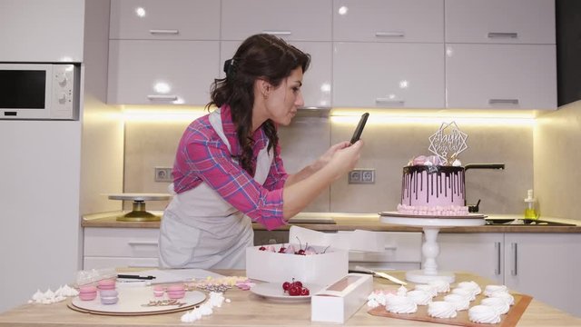 Female baker is taking a photo of a birthday cake. The woman has baked a delicious cookie at home for a gift.