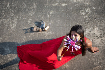 An young and attractive Indian brunette woman in red western dress enjoying with a pinwheel on the rooftop in a morning. Indian lifestyle and quarantine.