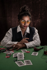 Young Indian Bengali brunette woman in vintage western suits playing cards on a casino poker table in brown textured copy space studio background. Indian lifestyle and fashion.