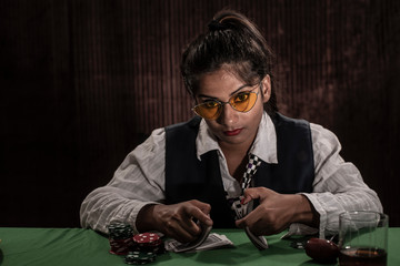 Young Indian Bengali brunette woman in vintage western suits playing cards on a casino poker table...