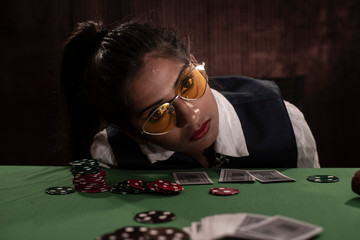 Young Indian Bengali brunette woman in vintage western suits playing cards on a casino poker table in brown textured copy space studio background. Indian lifestyle and fashion.