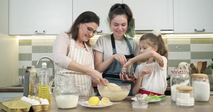 Mother teaches her two daughters cook muffins at home in kitchen
