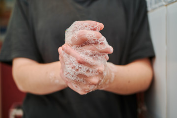 Hands washing with soap for coronavirus prevention by a young girl with a black t-shirt on a white tiled bathroom
