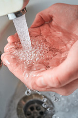 Fototapeta premium Hands holding water with big bubbles under the faucet while washing with light reflections on the palms for coronavirus prevention