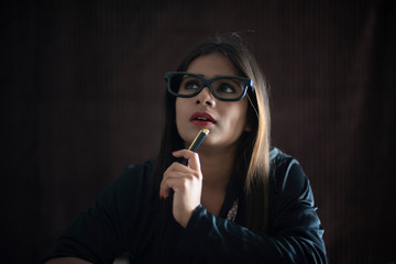 Obraz premium Portrait of an young Indian brunette girl in black corporate suit with a pen in dark copy space studio background. Indian lifestyle and corporate 