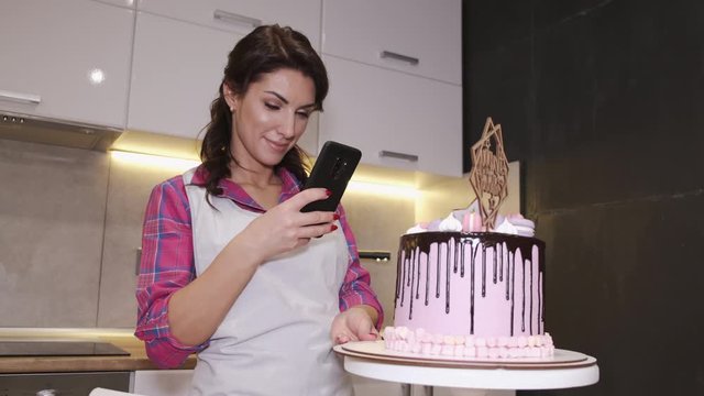 Female baker is taking a photo of a birthday cake. The woman has baked a delicious cookie at home for a gift.