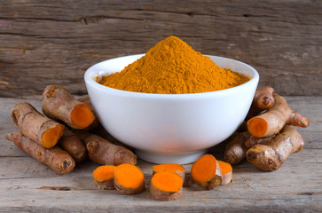 Turmeric powder in a white bowl and fresh turmeric (curcumin) on a wood background,Used for cooking and as herbal medicine.