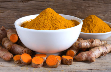 Turmeric powder in a white bowl and fresh turmeric (curcumin) on a wood background,Used for cooking and as herbal medicine.