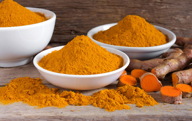 Turmeric powder in a white bowl and fresh turmeric  (curcumin) on a wooden table.