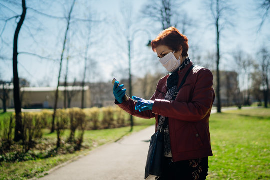 Senior elderly woman with protective cloth face mask/gloves walking outside.Coronavirus COVID-19 disease protection.Socialization restriction.Social distancing practice.Using smartphone to communicate