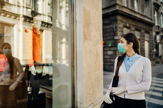 Woman With Mask Looking At A Closed Fashion Clothes Storefront.Clothing Shopping During Coronavirus Outbreak Shutdown.COVID-19 Quarantine Apparel Retail Store Closures.Small Business Loss Concept.