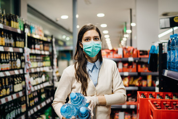 Woman with mask safely shopping for groceries amid the coronavirus pandemic in a stocked grocery...