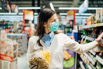 Shopper with mask safely shopping for groceries due to coronavirus pandemic in stocked grocery...
