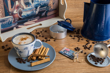 Cup of coffee, coffee beans, cinnamon sticks on a wooden table with tray and coffee filter.
