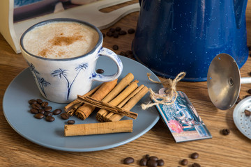 Cup of coffee, coffee beans, cinnamon sticks on a wooden table with tray and coffee filter.