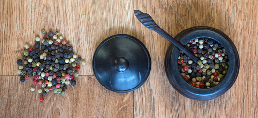 Pepper corns and a wooden pot.  Red, black and green peppers in a pot on a wooden table.