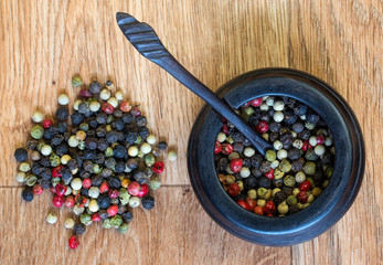 Pepper corns and a wooden pot.  Red, black and green peppers in a pot on a wooden table.
