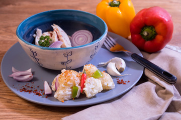 Chicken, potato salad dish served on a blue plate and handmade bowl.  Decorated with red, yellow peppers and chillies. 