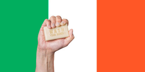 Caucasian male hand holding soap with words: Wash Your Hands against an Irish flag background