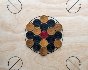 Carrom men and red arranged on the board around the center star.