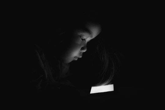 A young Asian woman is sleeping, watching mobile phones in the dark.