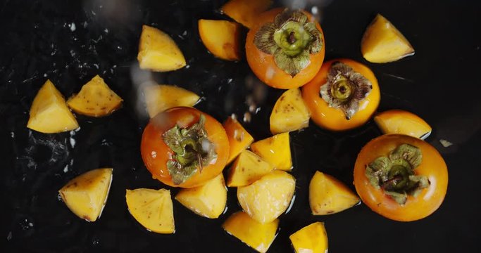 On whole and slices of persimmon falling water drops.