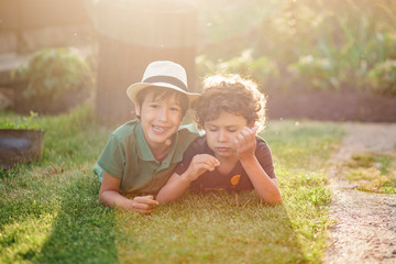 Two brothers lying on the grass in a park outdoors, smiling and laughing